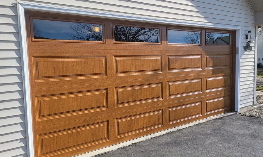 Wood-grain composite garage door with top windows on a residential garage