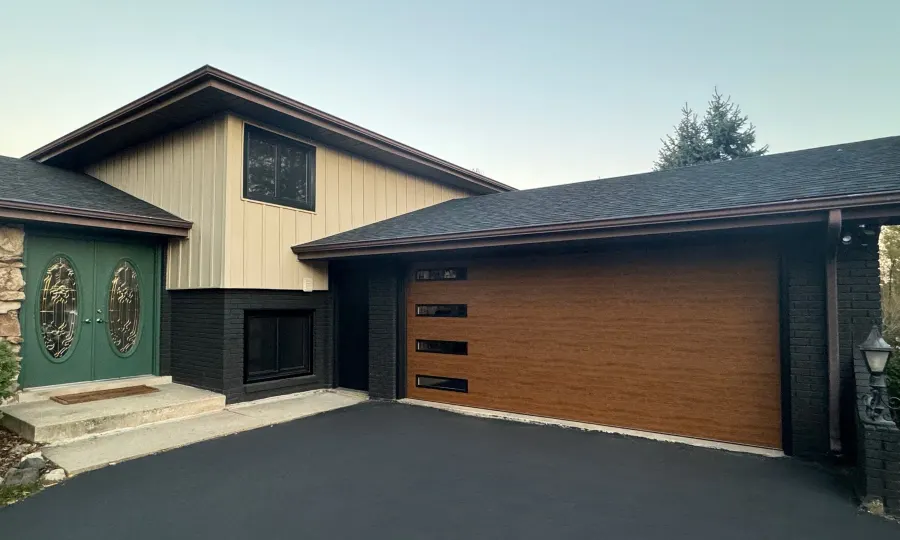Modern wood-tone garage door with horizontal glass panels on a residential home