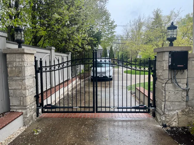 Black ornamental swing gates with stone pillars, LiftMaster operator, and pillar-mounted access control — finished install in Chicagoland.
