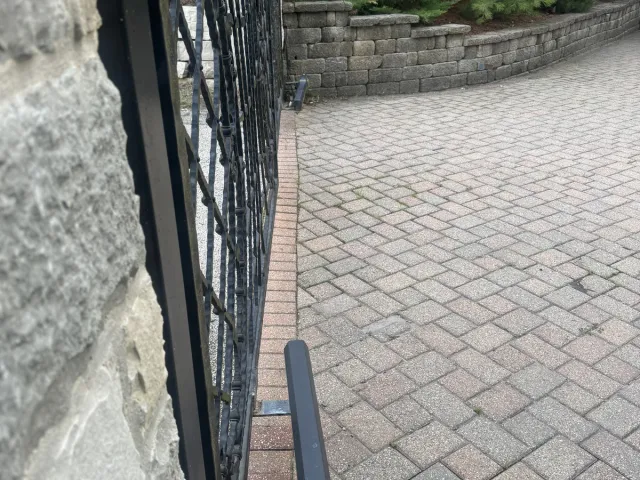 Black ornamental gate on a paver-brick commercial entry — sized for delivery vehicles and configured with a vehicle detection loop in the approach.