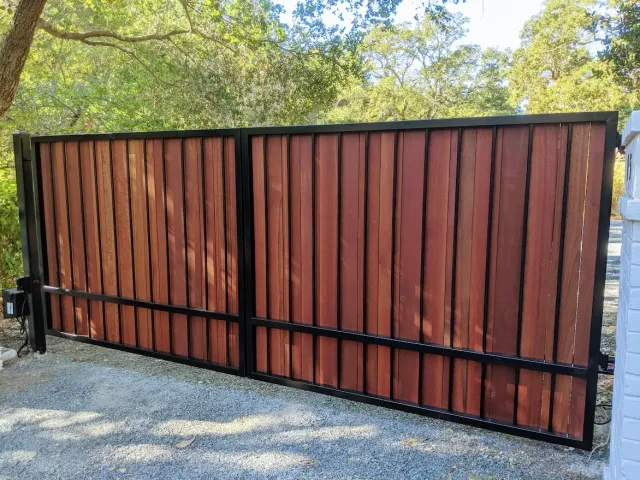 Side profile of the same custom wood-and-iron gate, showing the panel construction and operator arm tucked behind the masonry pillar.