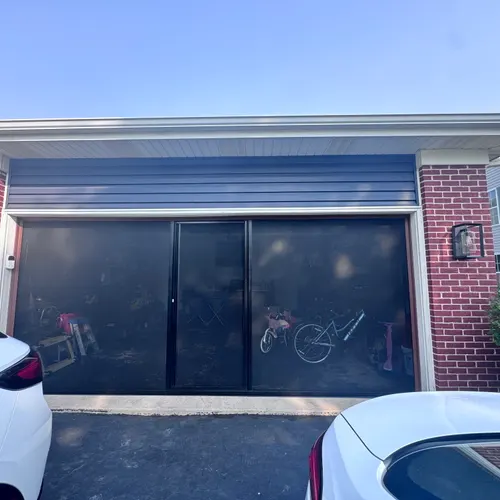 Lifestyle Screen fully extended across a 2-car garage opening — fine black mesh, clear view to bikes inside