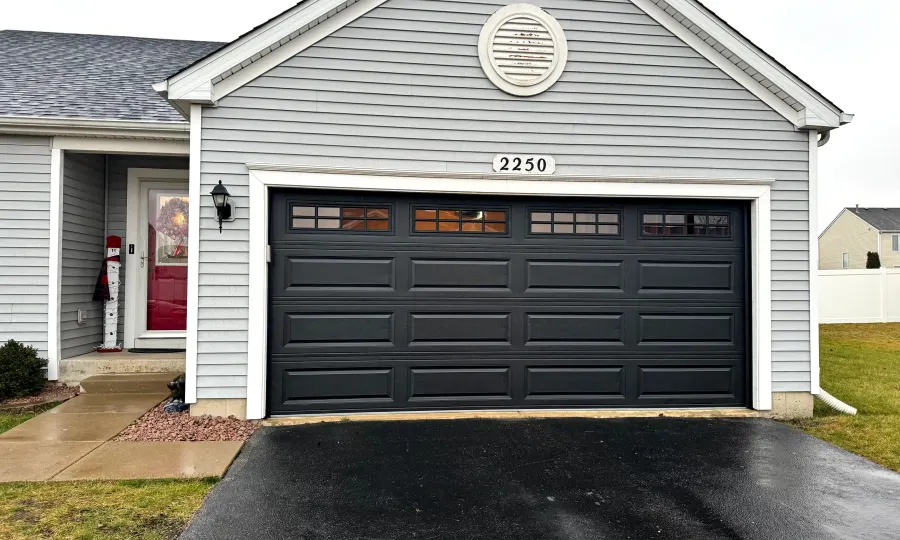 Black carriage-style garage door with top row of square windows on a gray-sided suburban home