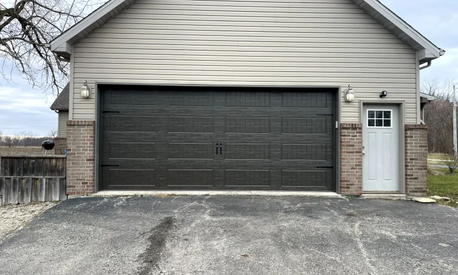 Black raised-panel steel garage door on a Chicago-area home with tan siding and brick base