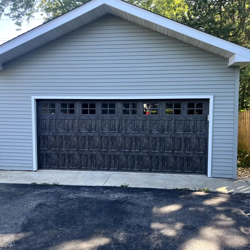 Raised-panel garage door install on a light-blue sided home