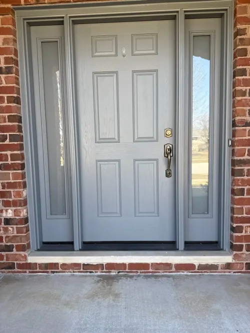 Gray six-panel entry door with sidelights on a red-brick home