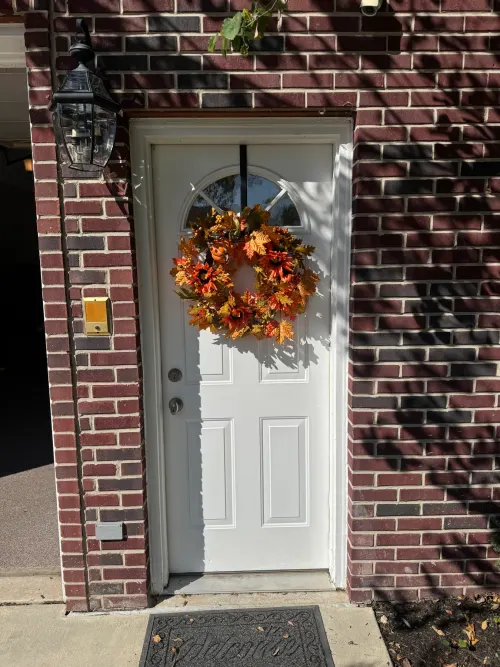 White entry door with a fall wreath, red-brick home