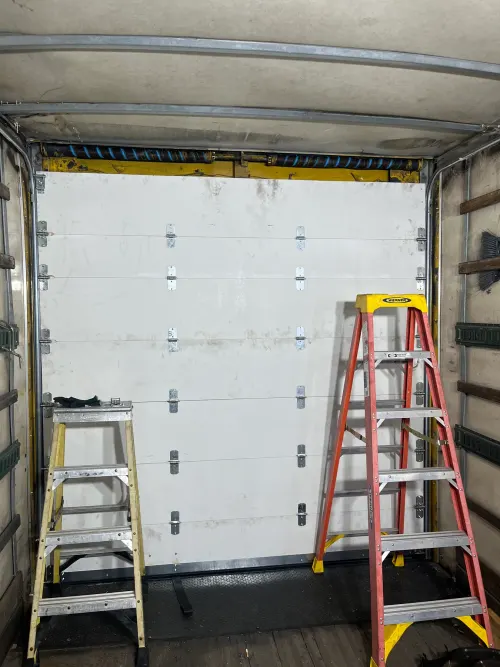 Ladder set up inside a box truck cargo area during a roll-up door install