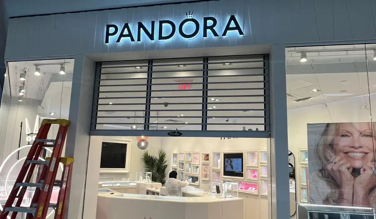 A repaired commercial overhead door at a Pandora store, partially open, with a worker inside and a ladder nearby.