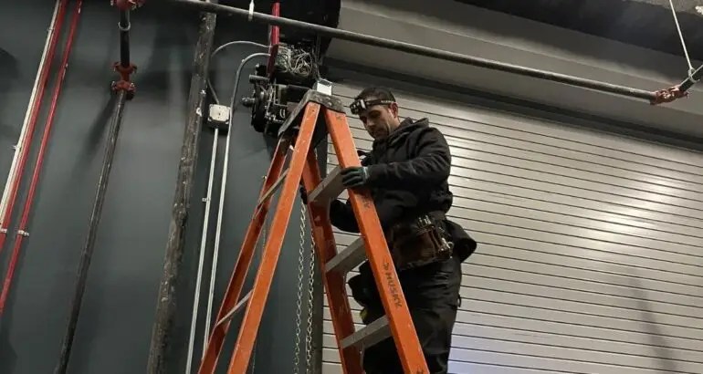 Technician performing commercial door repair on a large industrial garage door.