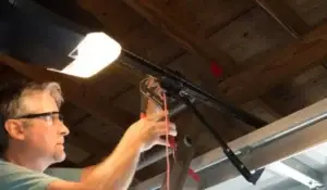 A technician performing commercial overhead door repair, adjusting components on a ceiling-mounted garage door opener system.