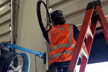 The man wearing the safety vest installing the garage door as part of a comprehensive garage door repair and maintenance service.