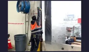 Technician in safety vest using tools to repair a damaged garage door in an industrial warehouse