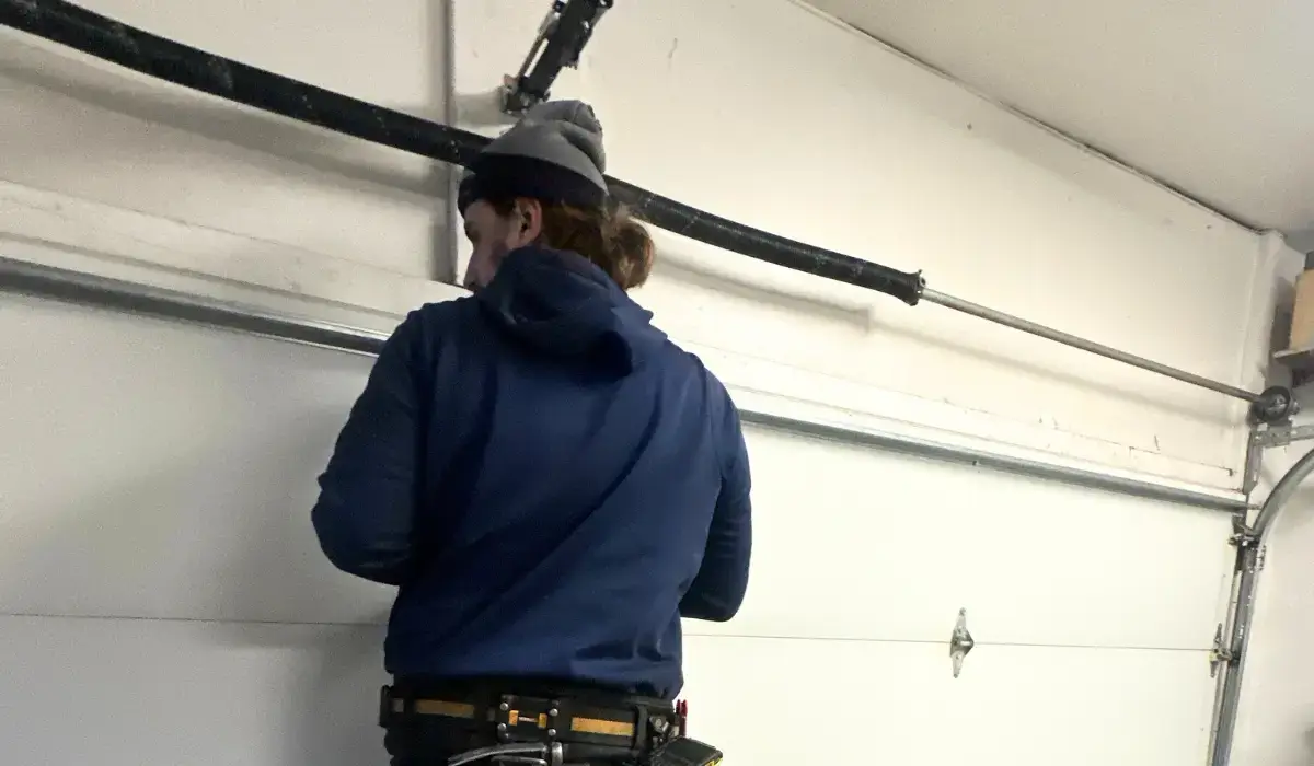 Technician in a blue hoodie fixing a garage door stuck due to a broken spring in a garage.
